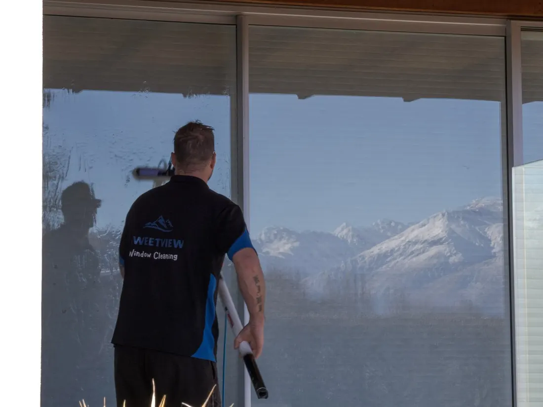 Mike cleaning full-height glass in Wanaka, mountains reflected
